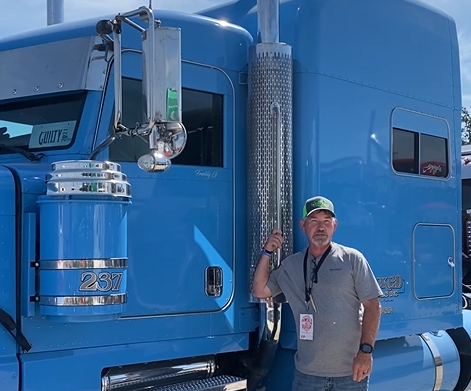 Truck owner standing beside a blue semi truck
