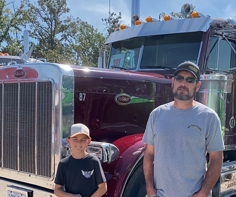 Man and child standing in front of a maroon semi truck
