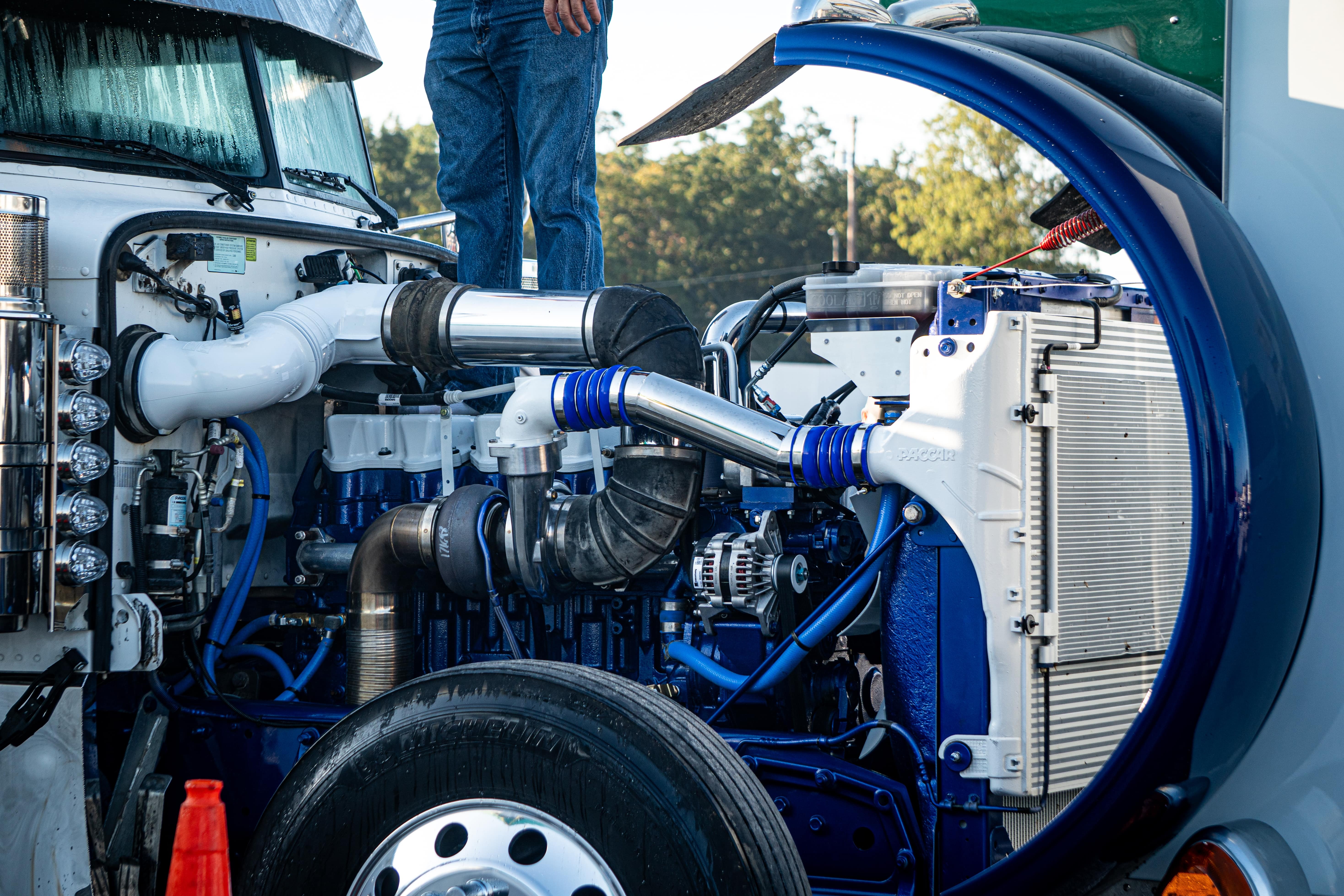 Truck driver standing on open semi truck hood with exposed engine components